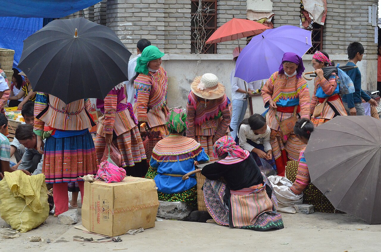 Flower H'mong women in bright traditional dress with umbrellas at a busy northern Vietnam ethnic market