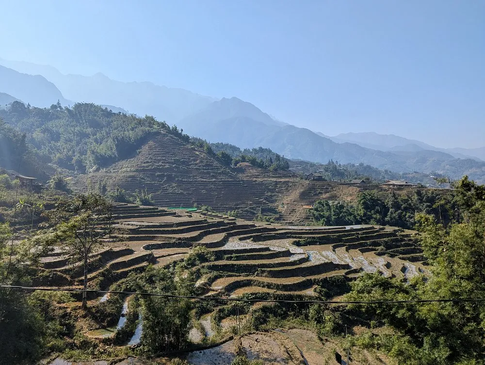 Cut and harvested rice terraces in late October under clear skies, with layered mountain ridges toward Fansipan behind the Muong Hoa Valley, Sapa