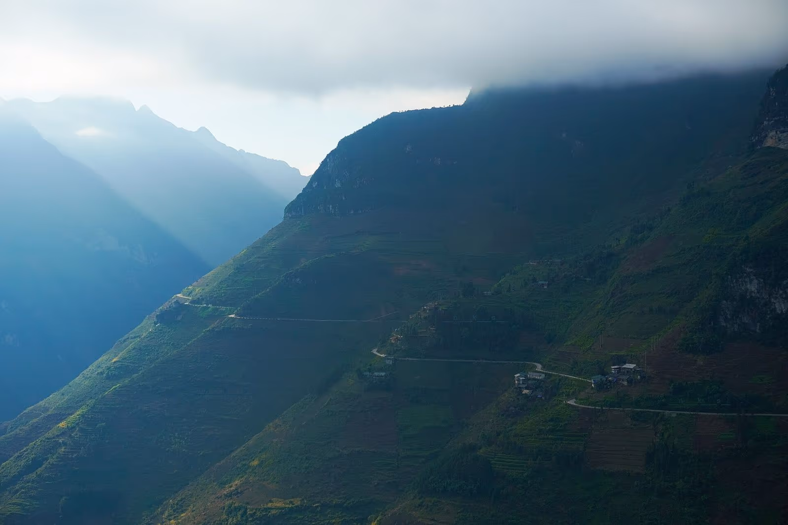 Steep slope of the Ma Pi Leng pass with thin mountain roads and a few houses under low cloud