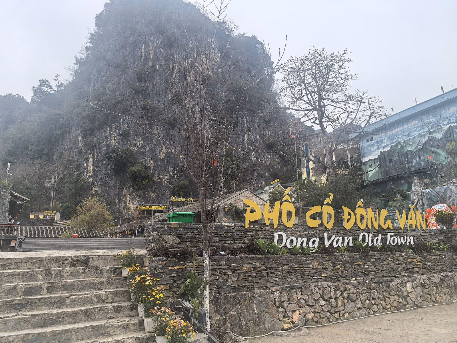 Entrance sign of Dong Van Old Town below a misty limestone cliff