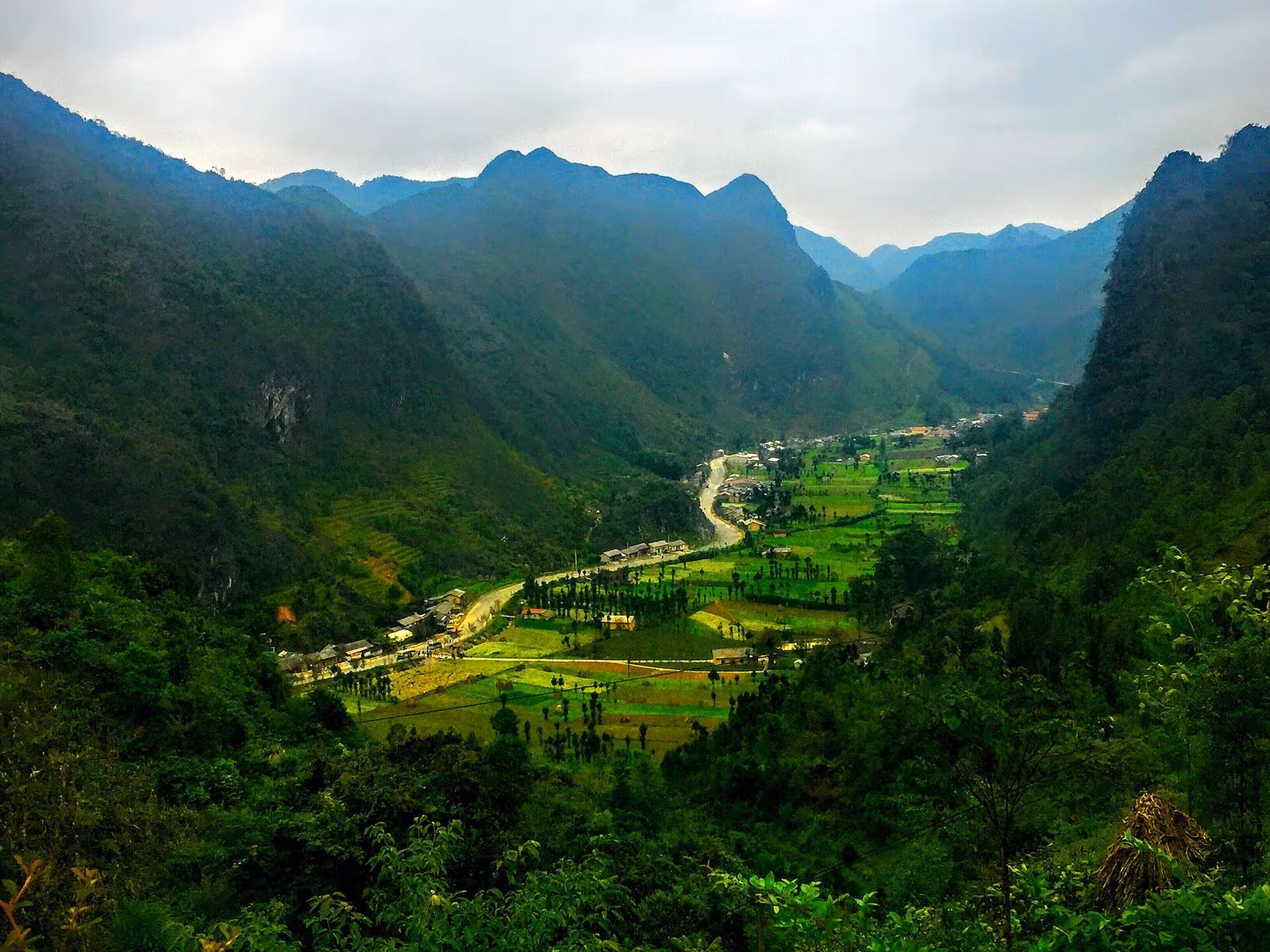 Looking down a narrow green valley with a road, houses and small fields at Sung La, Dong Van