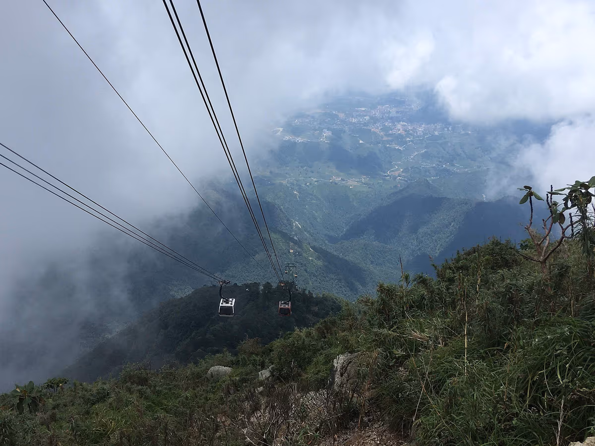Two cable car gondolas climbing through cloud above Sapa town seen far below