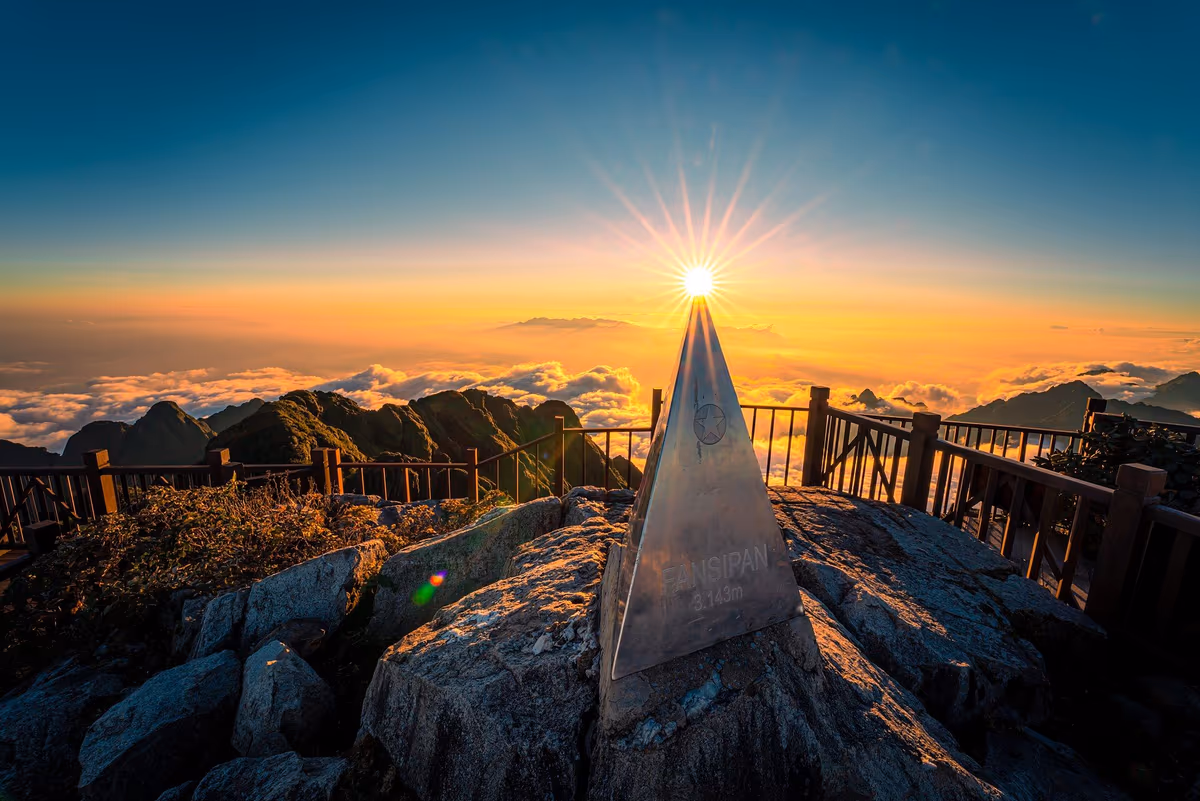 The Fansipan summit marker engraved 3,143 m with a sea of clouds below the railing and a sun-star in the sky