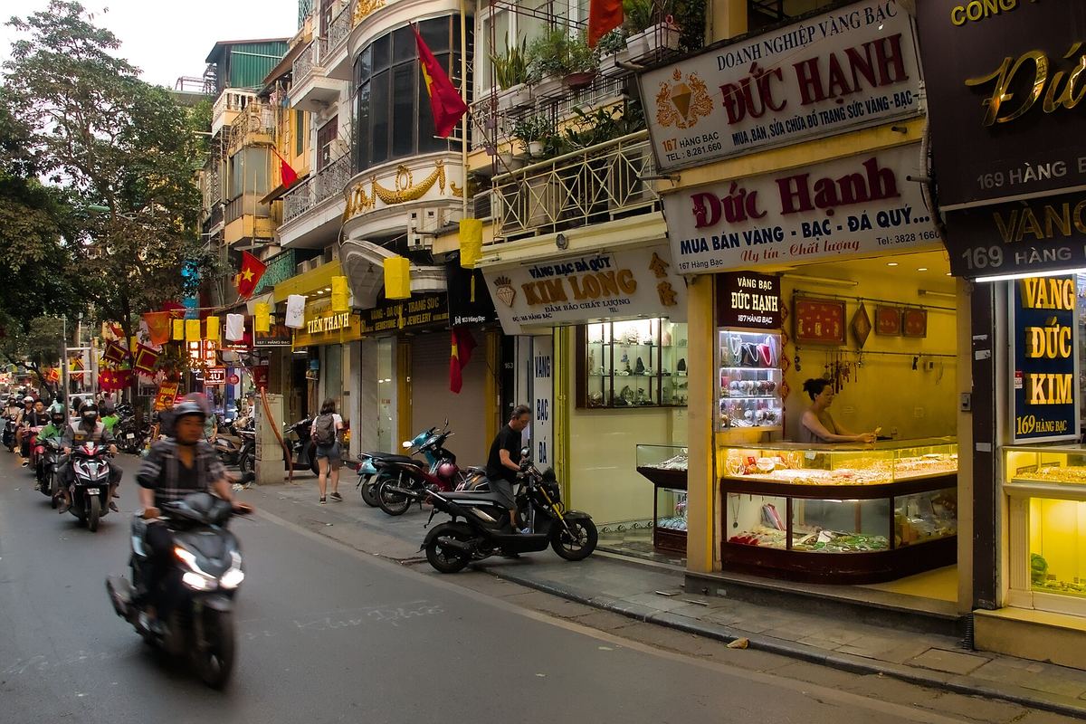 Hang Bac Street in Hanoi's Old Quarter, a row of gold and silver jewellery shops with motorbikes passing on the road