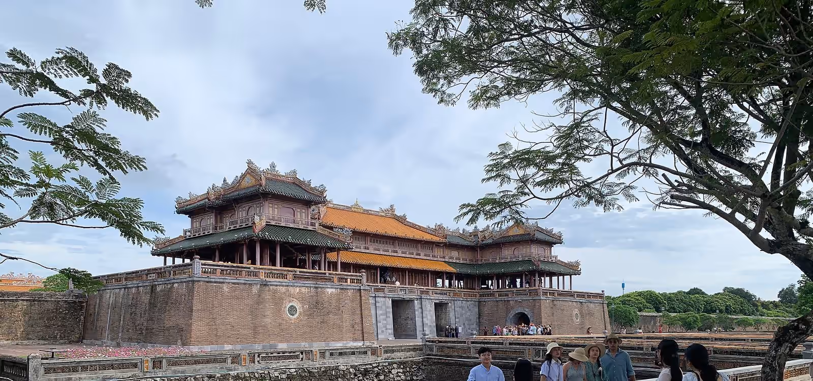 The two-storey Ngo Mon (Meridian) Gate of the Hue Imperial City with its orange roof, behind a stone-walled moat and a tiled terrace