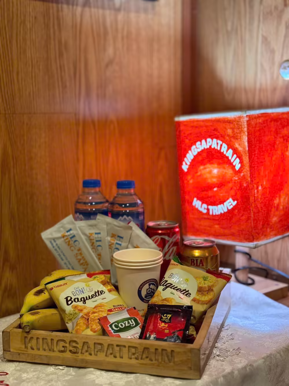 King Sapa Train welcome tray — a wooden crate with bananas, snacks, Cozy tea, water and a can of local beer