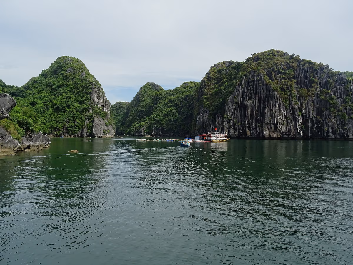 Green limestone karsts rising from calm water in Lan Ha Bay with a small boat anchored below the cliffs