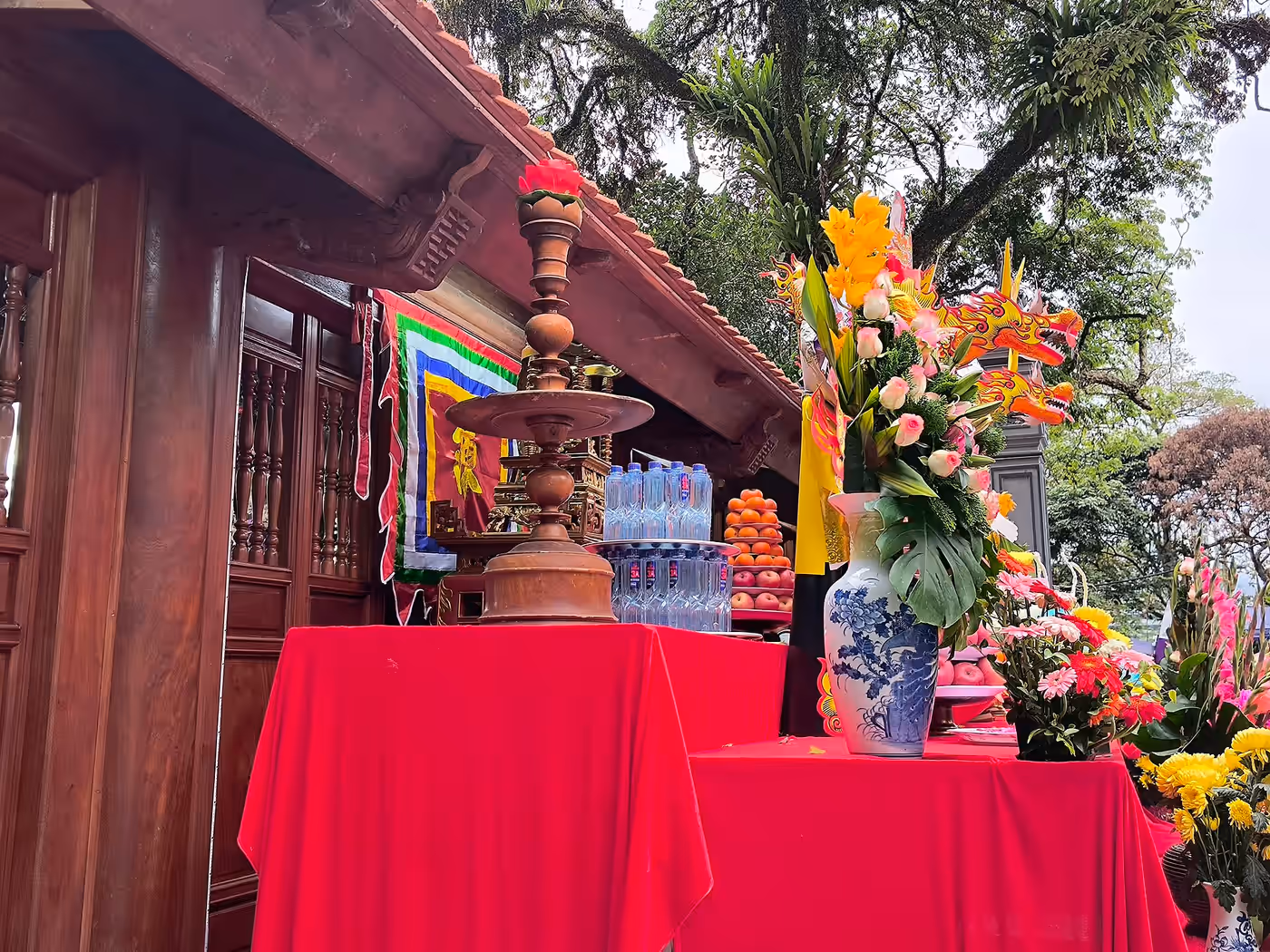 A temple veranda with red-cloth altar tables, offering flowers and a golden dragon decoration