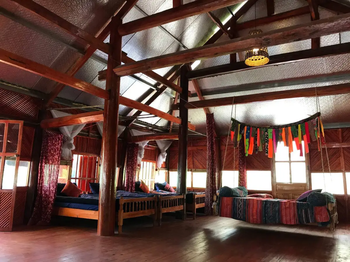 Traditional Black H'mong homestay interior in Ta Van village, Sapa — wooden beams, colorful textile bedding, morning light