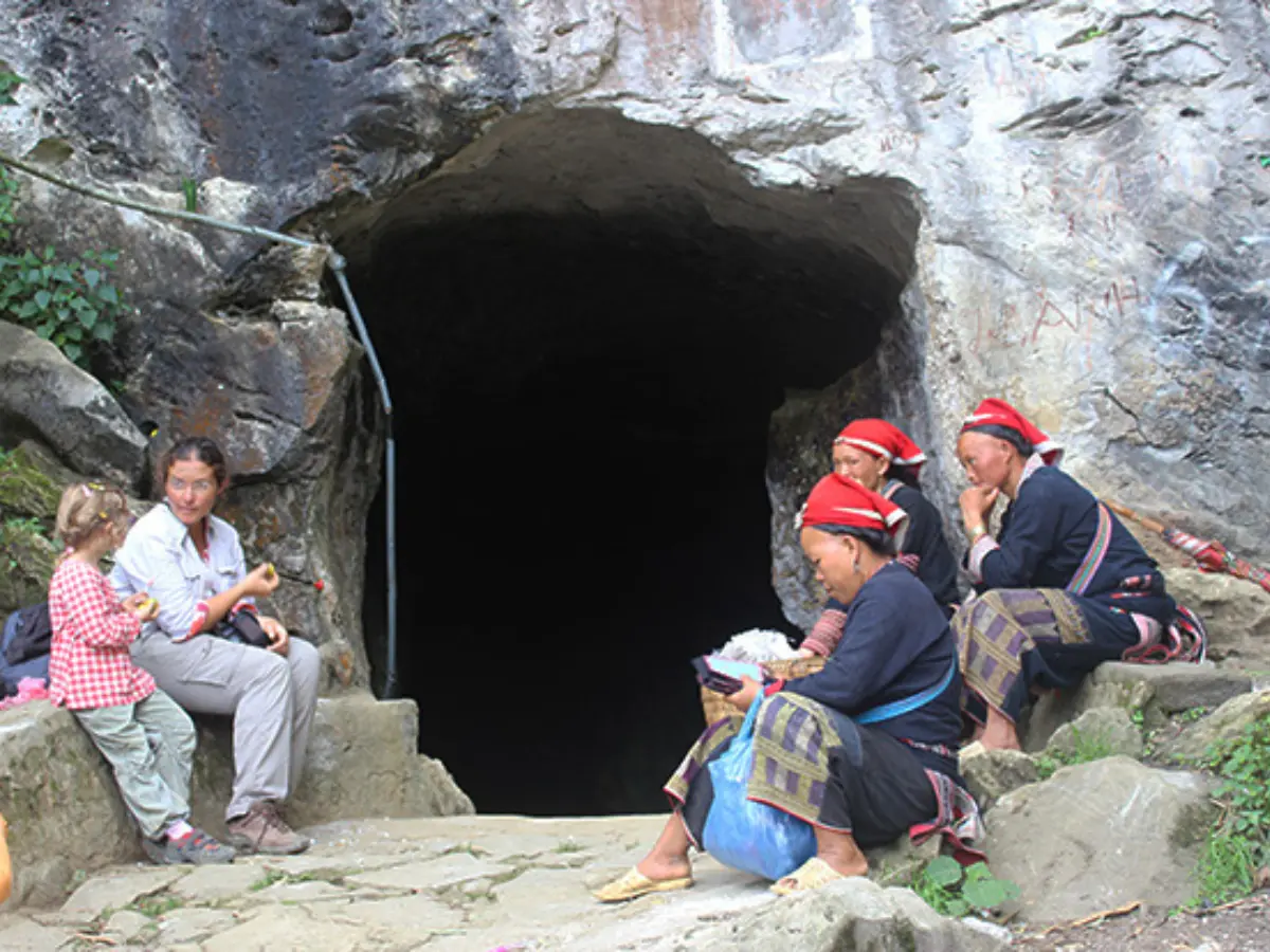 Red Dao women in traditional red headdresses and embroidered clothing at a cave entrance near Ta Phin, Sapa