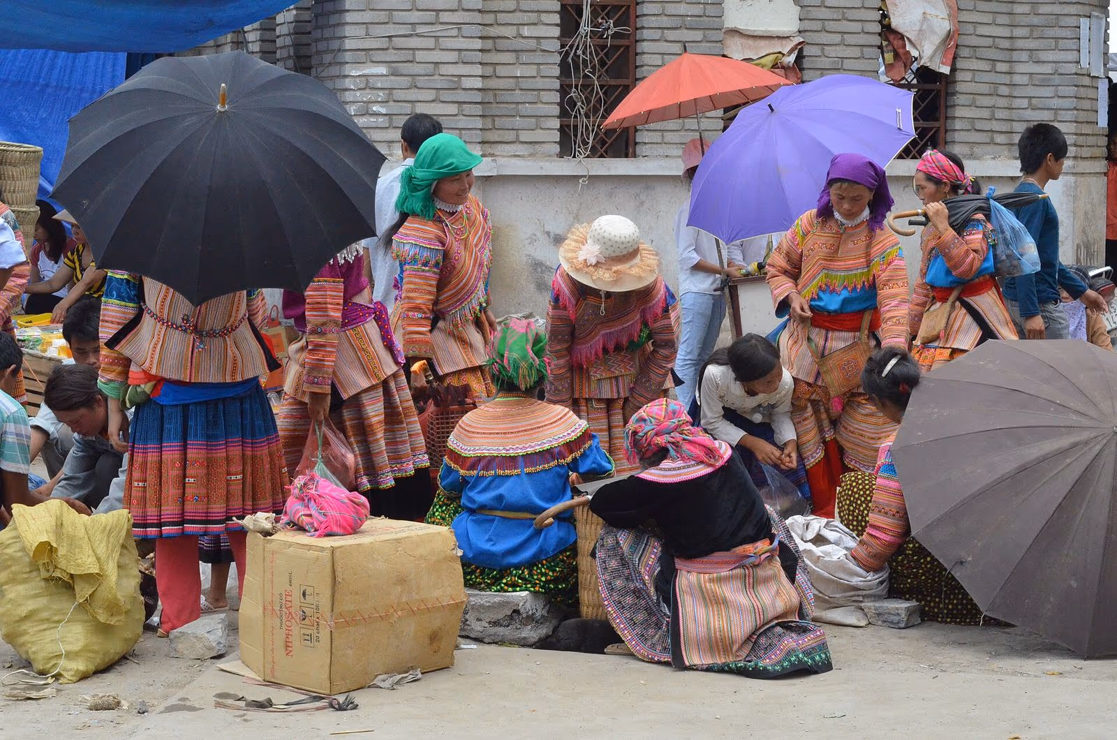Flower H'mong women in embroidered costumes and umbrellas at Bac Ha market