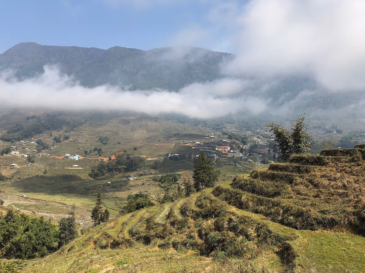 A low band of cloud lying across a terraced valley near Sapa with houses below and a mountain above