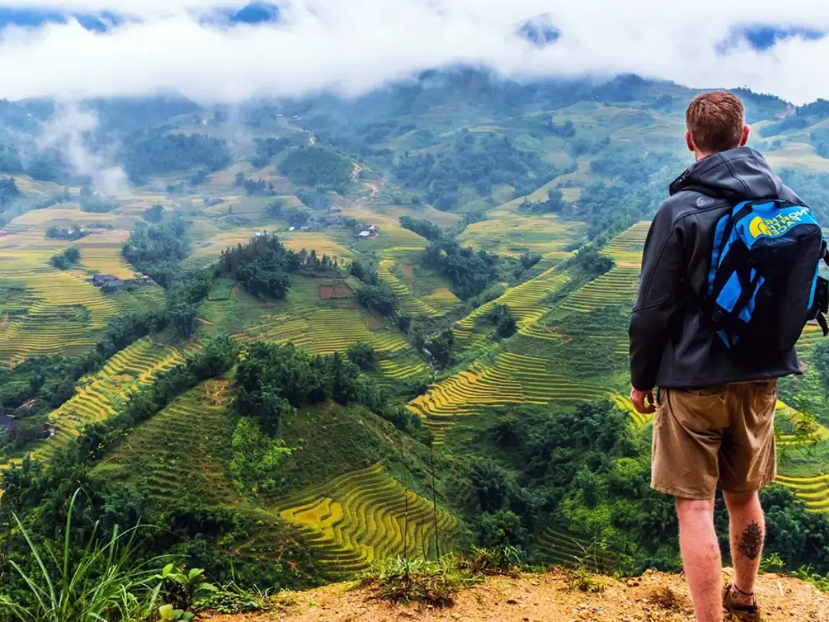Panoramic view of Muong Hoa Valley from high ridge, showing layered golden rice terraces cascading down steep mountain slopes under clouds, Sapa, Vietnam