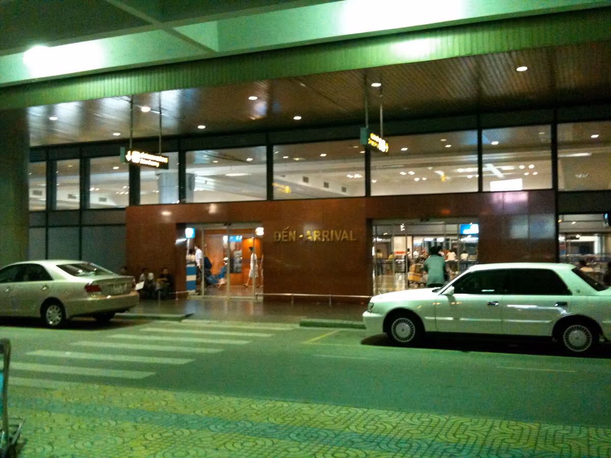 The arrivals entrance of Noi Bai airport at night, with the sign Den - Arrival over the doors and two parked cars