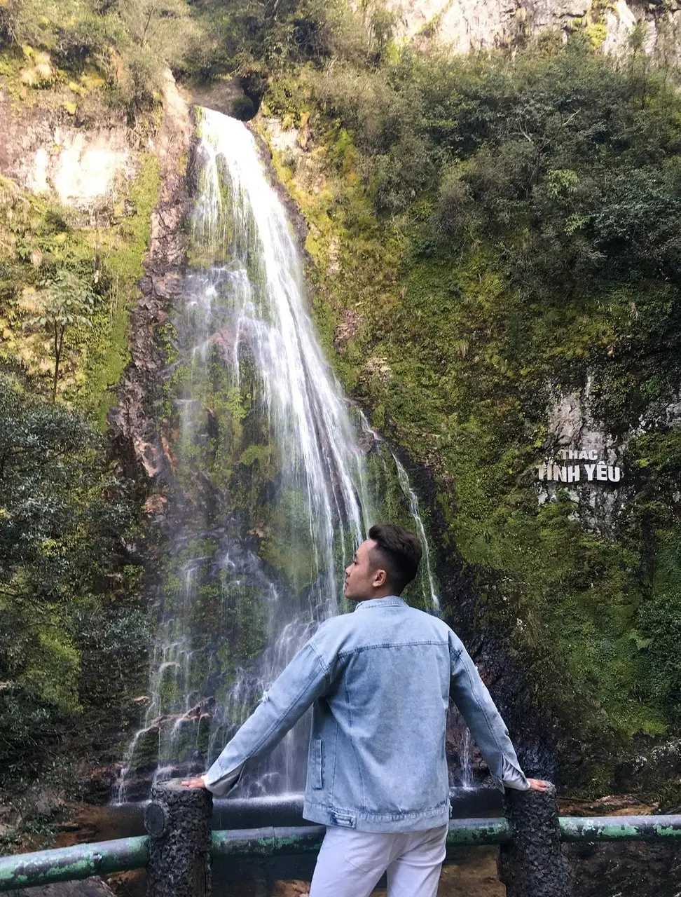 A visitor at the viewing rail in front of Love Waterfall, with the Thac Tinh Yeu sign carved into the cliff face