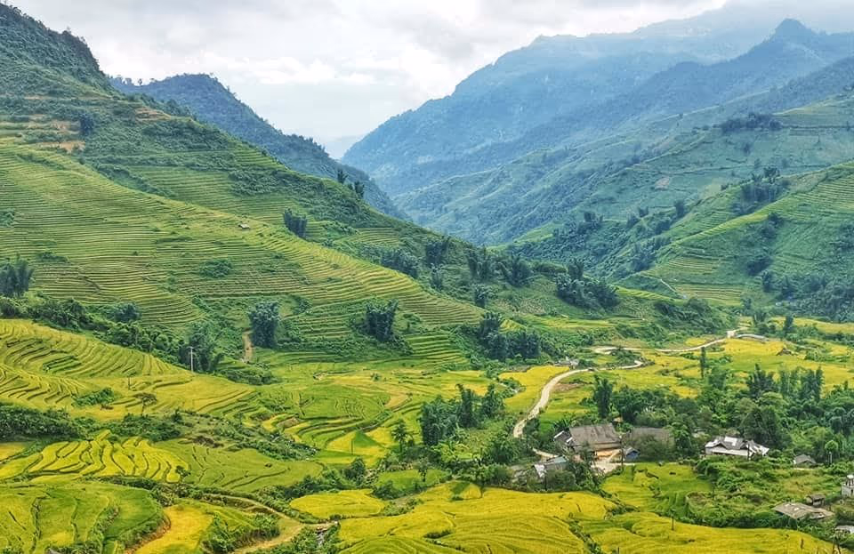 A terraced valley at harvest colour with a small hamlet and a track below layered mountains at Y Ty